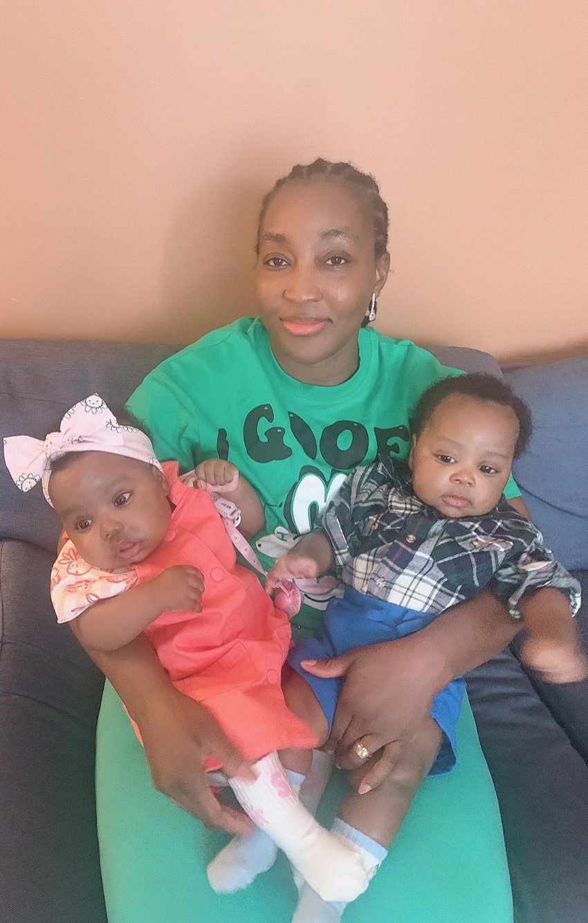 Zeinab at home on the sofa, holding her twin babies